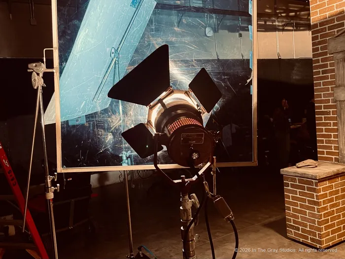 A fresnel light with its barn doors open, burning through a diffusion frame on set